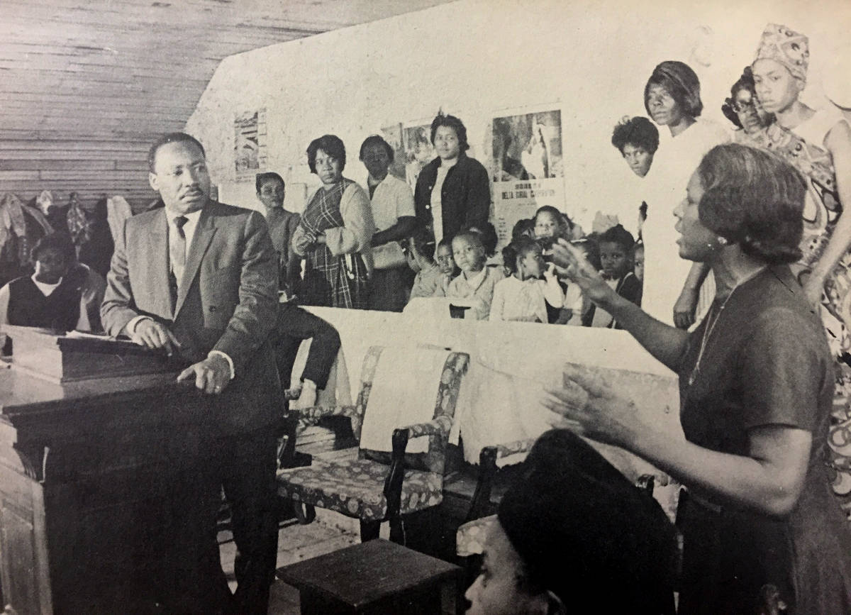 Rev. Dr. King listens as a woman speaks in a crowded classroom.